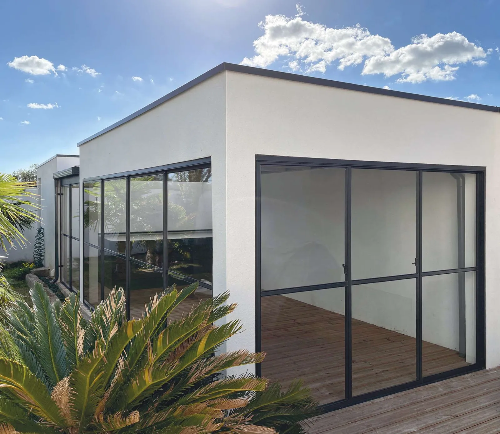 Extension contemporaine en enduit blanc, grandes baies vitrées en aluminium noir, terrasse en bois