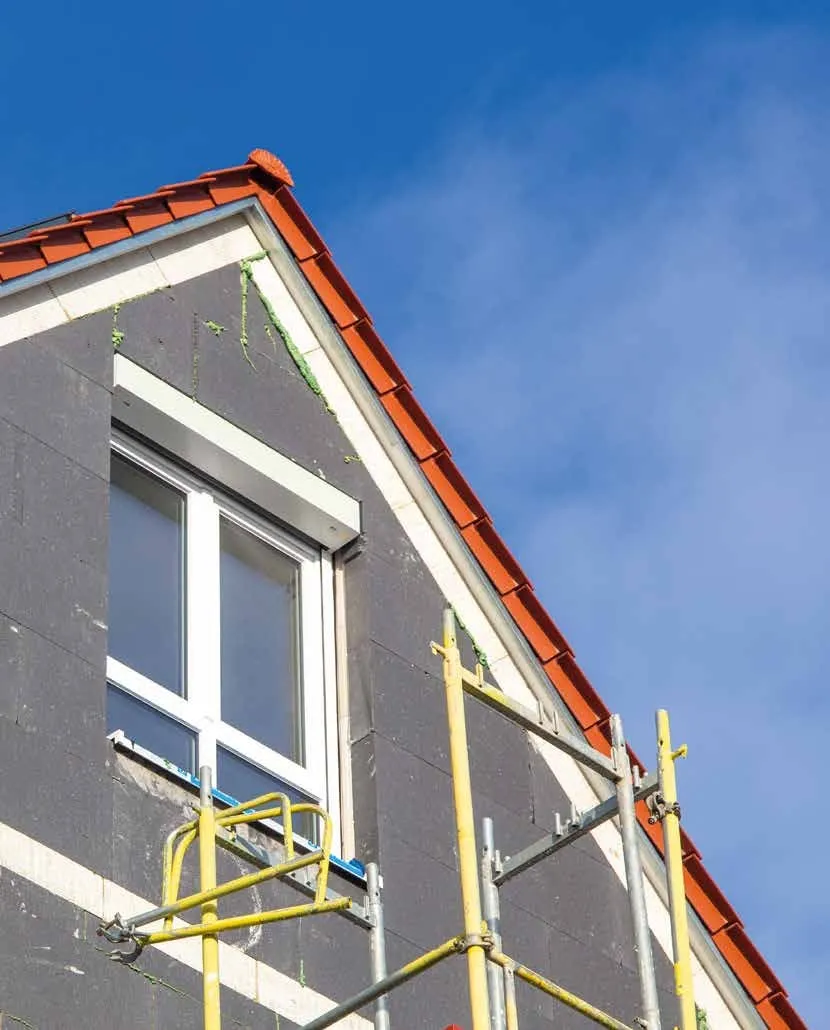Pignon de maison en cours d'isolation par l'extérieur, échafaudage et fenêtre neuve à coffre de volet roulant