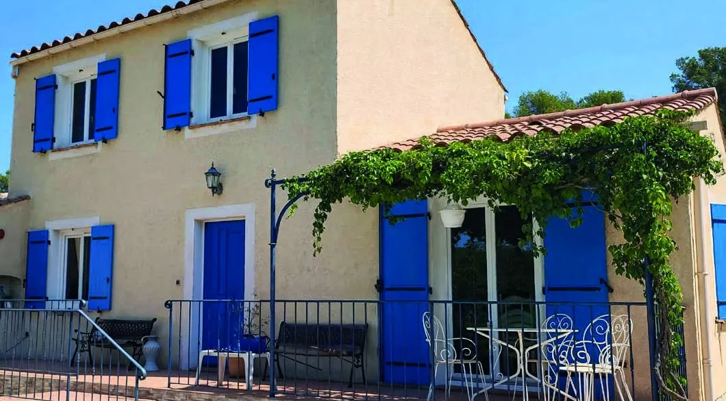 Maison provençale en crépi ocre, fenêtres PVC blanches et volets bleus, en plein soleil