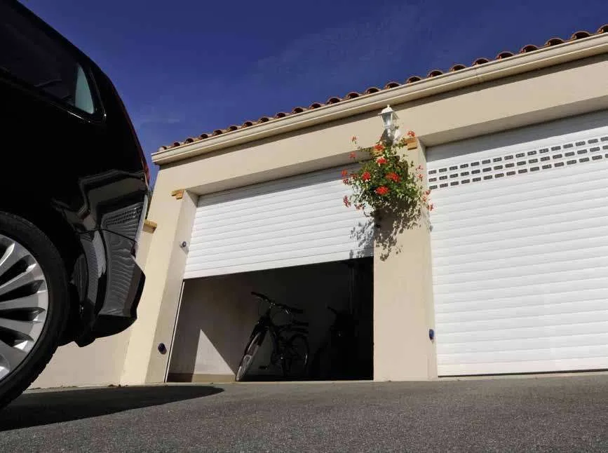 Deux portes de garage enroulables blanches sur une maison aux tuiles rondes, une voiture garée devant