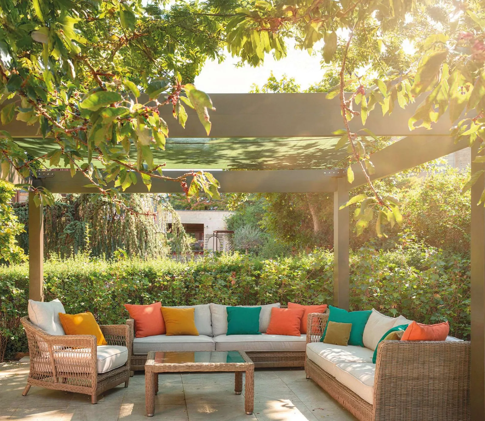 Pergola bioclimatique dans un jardin arboré, salon de jardin aux coussins colorés