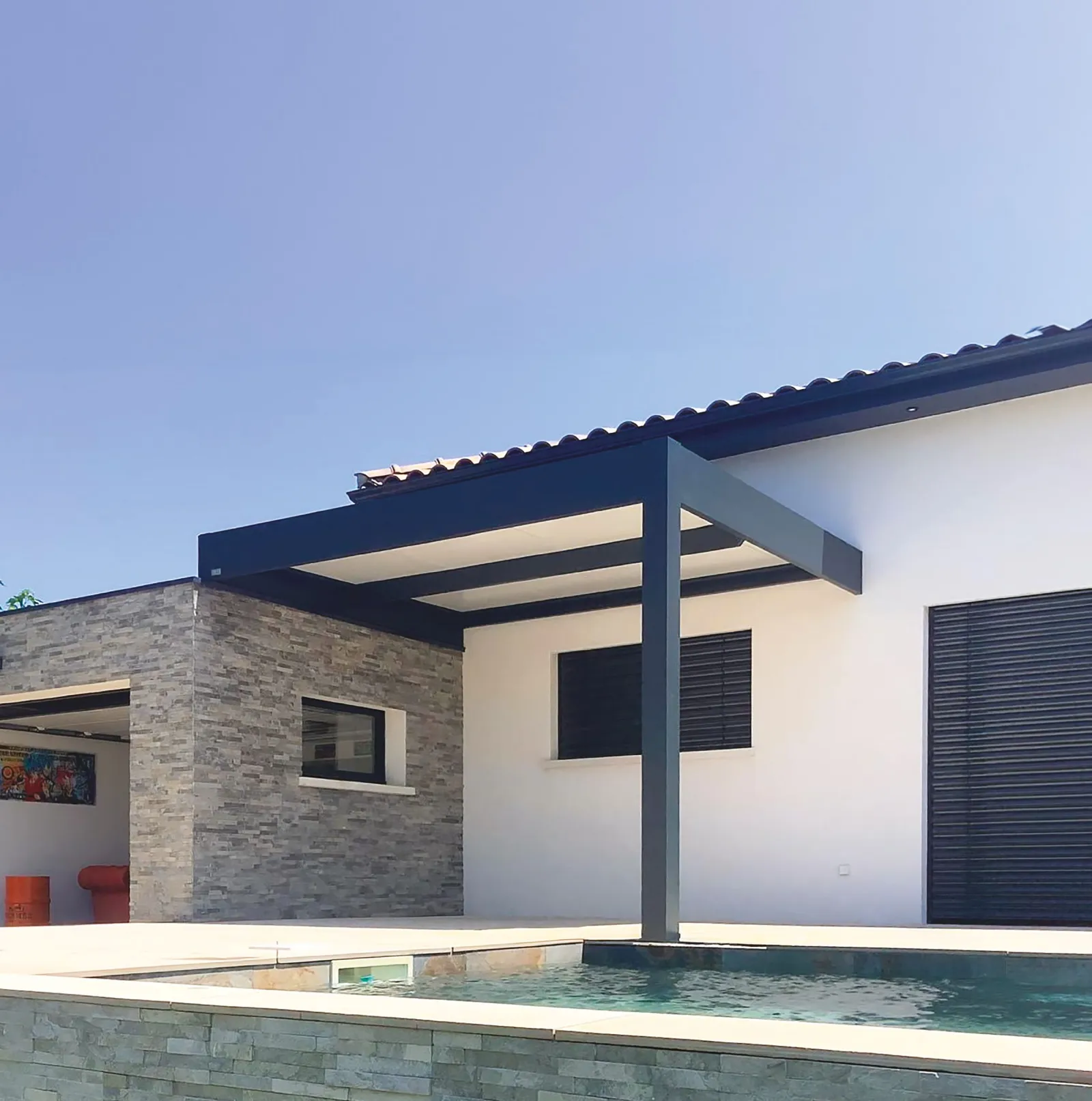Pergola aluminium anthracite adossée à une maison blanche, au bord de la piscine, sous un ciel bleu