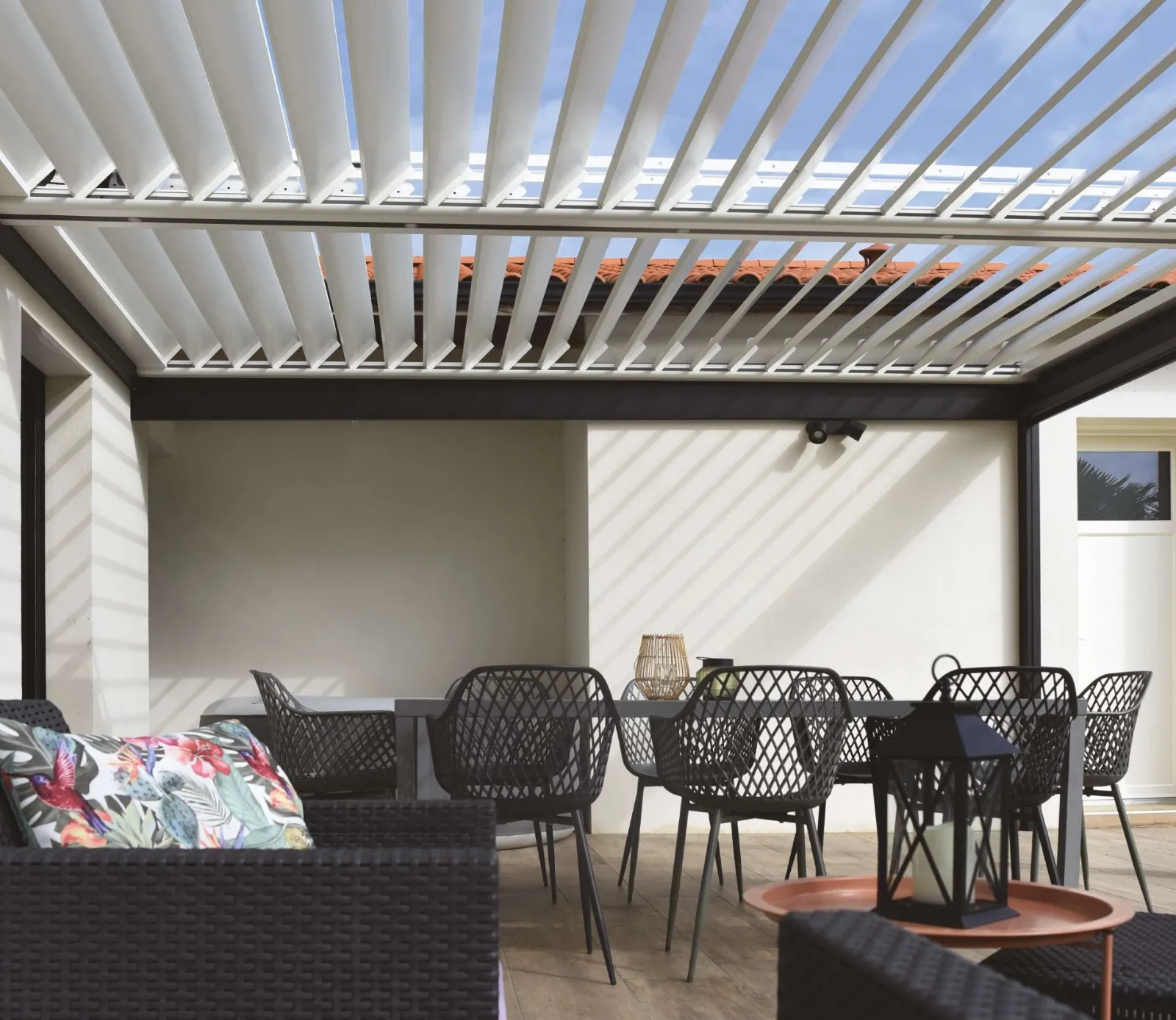 Vue sous une pergola bioclimatique aux lames ouvertes, table et chaises de jardin