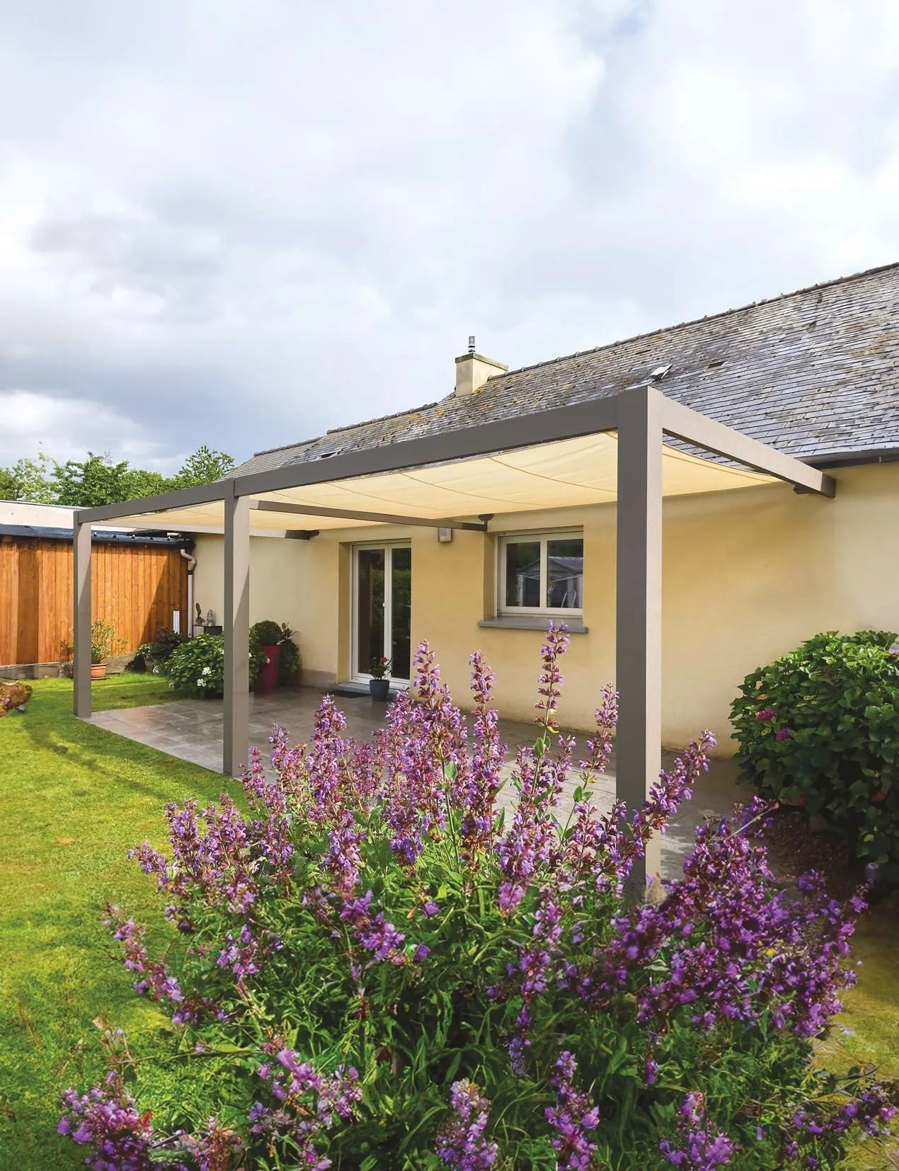 Pergola en aluminium gris clair adossée à une maison de plain-pied, massif de lavande en fleurs