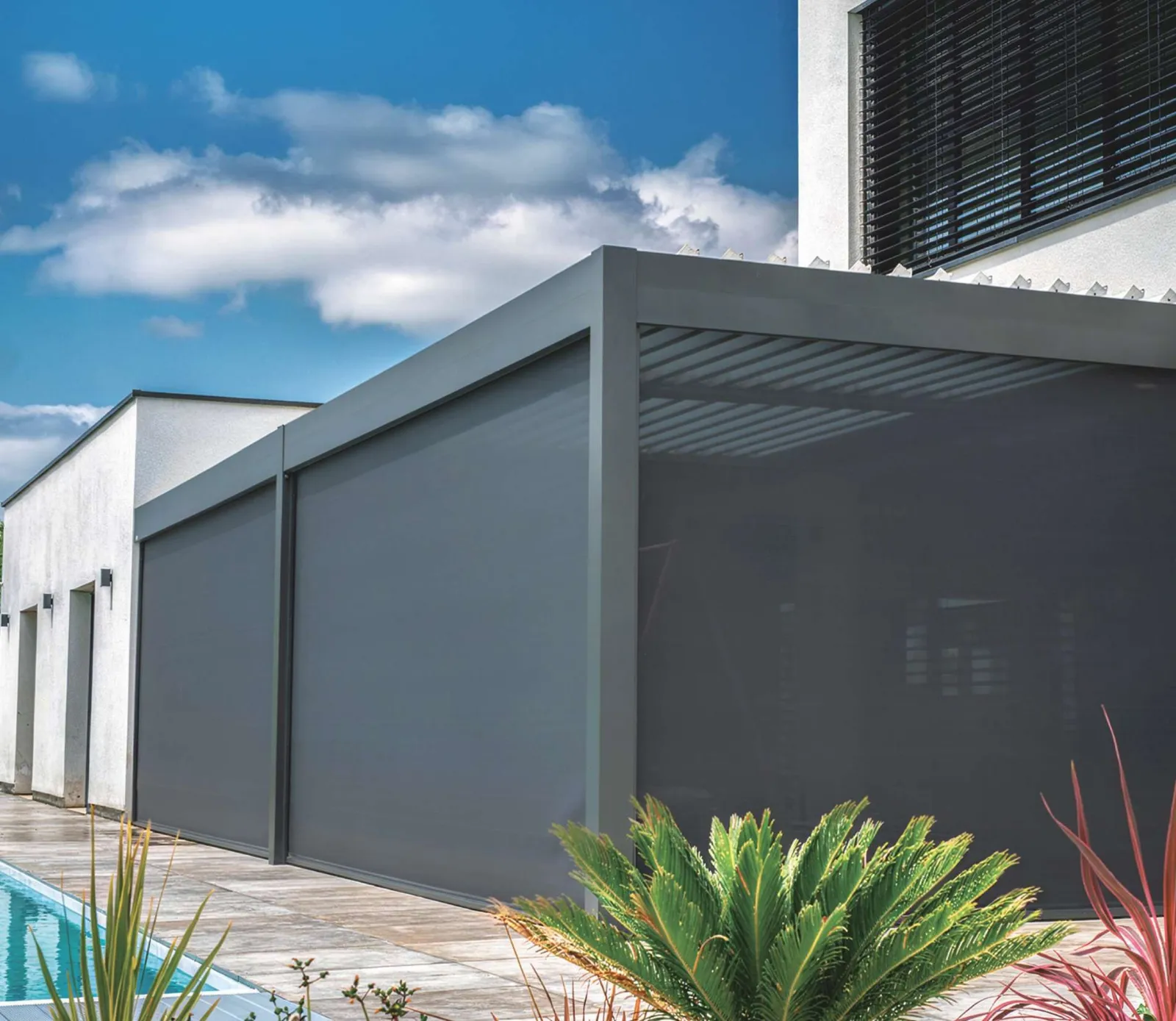 Pergola en aluminium anthracite fermée par des stores screen, au bord d'une piscine