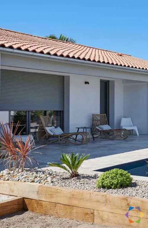 Maison de plain-pied aux tuiles rondes, volets roulants blancs relevés sur les baies, terrasse au bord de la piscine